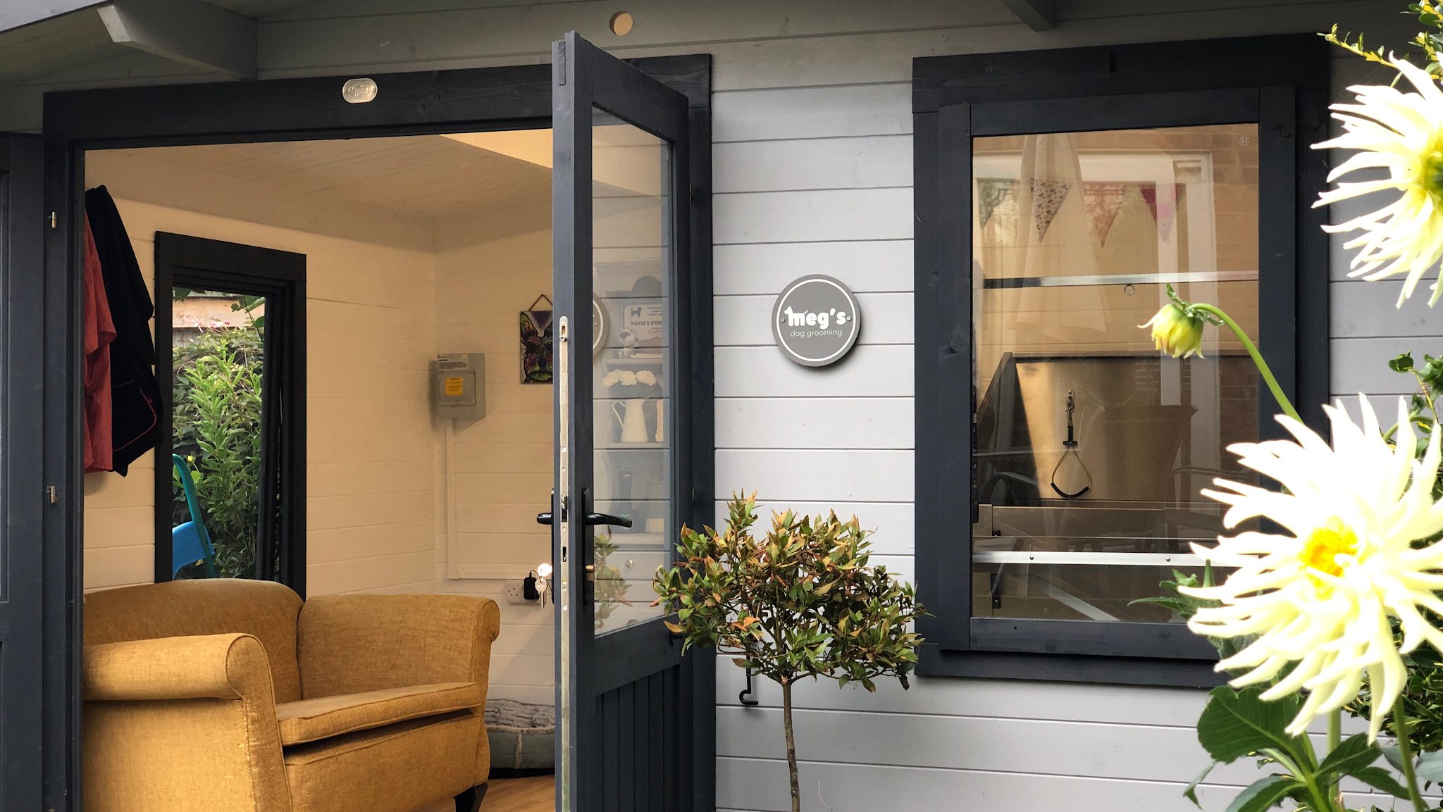 The Meg's Dog Grooming studio with its round sign, French doors open onto the garden